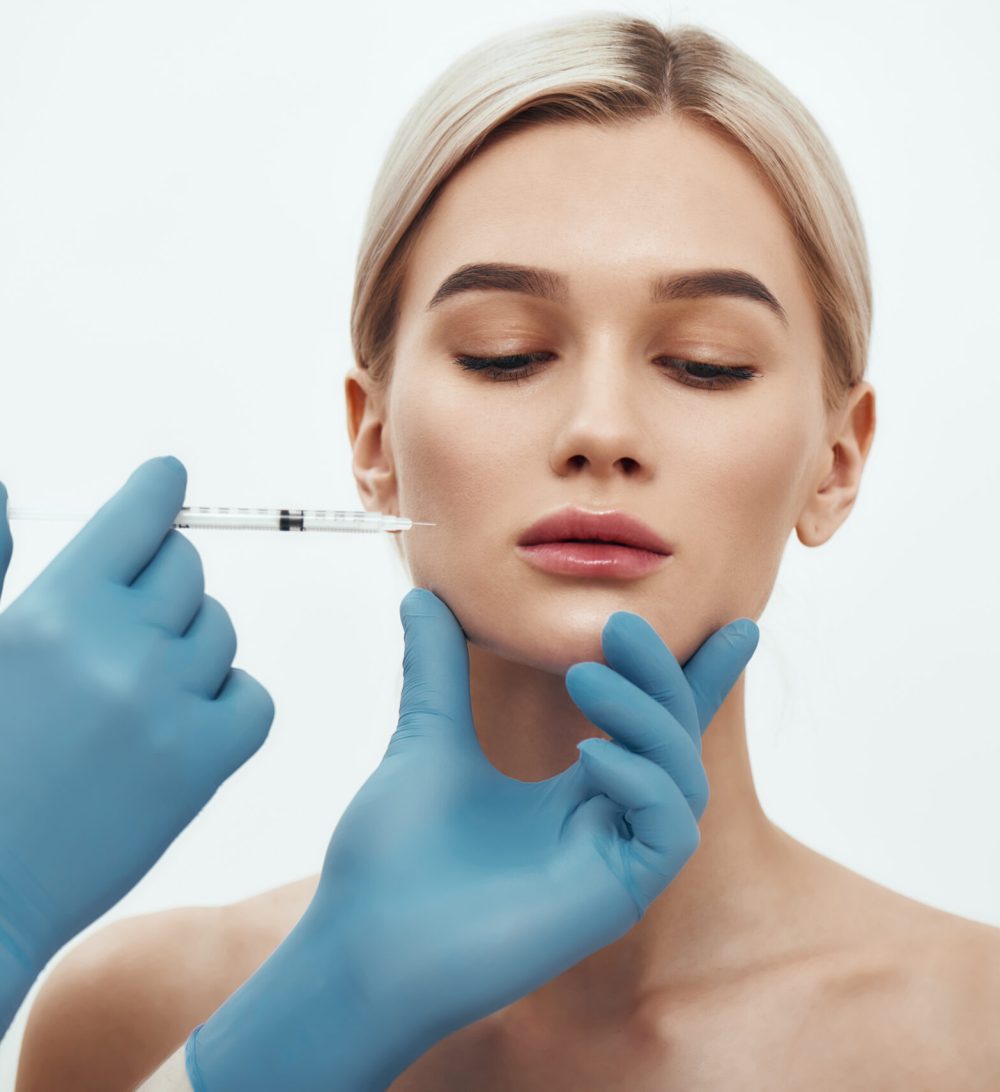 Botox injection. Young attractive woman keeping her eyes closed while doctors hand making an injection in her face. Studio shot. Beauty concept