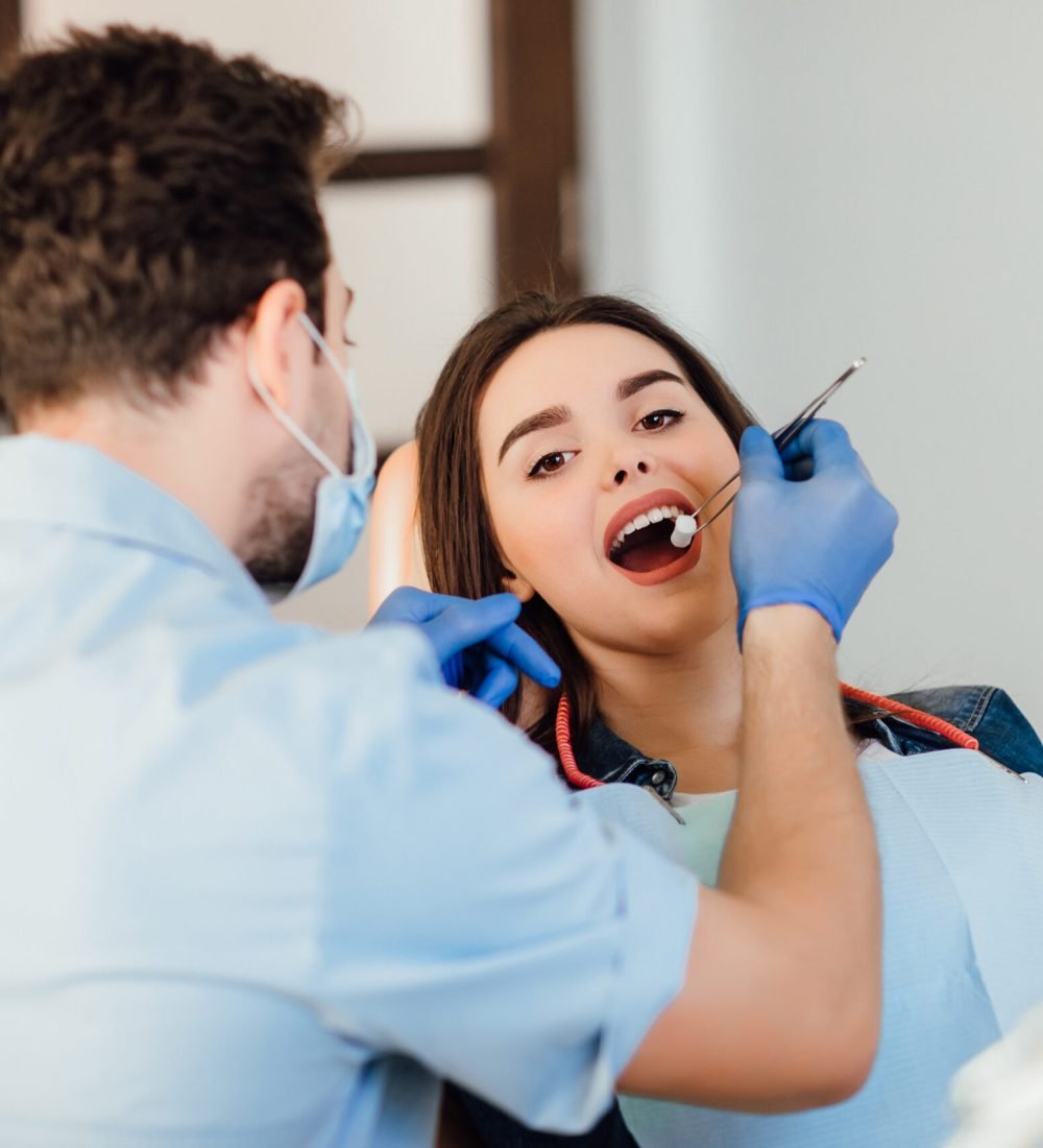 Dentist making professional teeth cleaning withb the cotton, female young patient at the dental office.